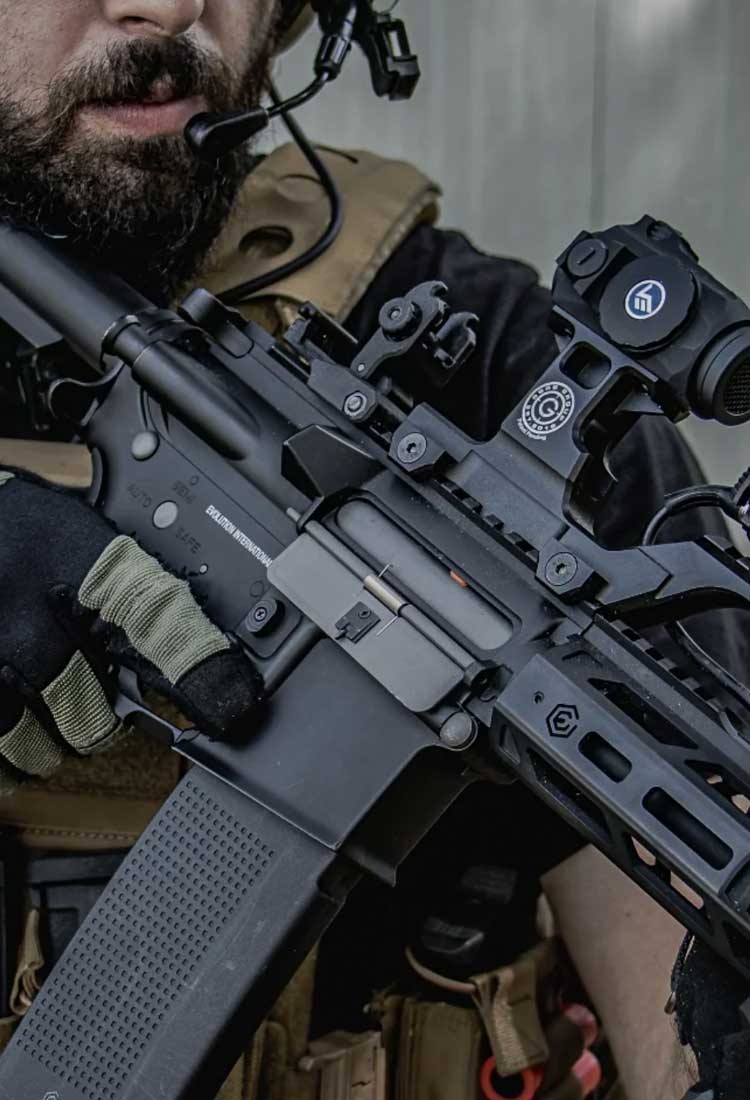 Person holding an Evolution Airsoft rifle with tactical gear in a close-up shot